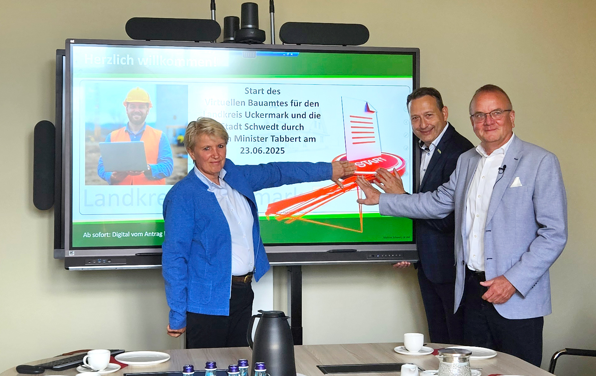 Foto: 3 Personen halten eine Hand an den virtuellen Startknopf auf einem Bildschirm