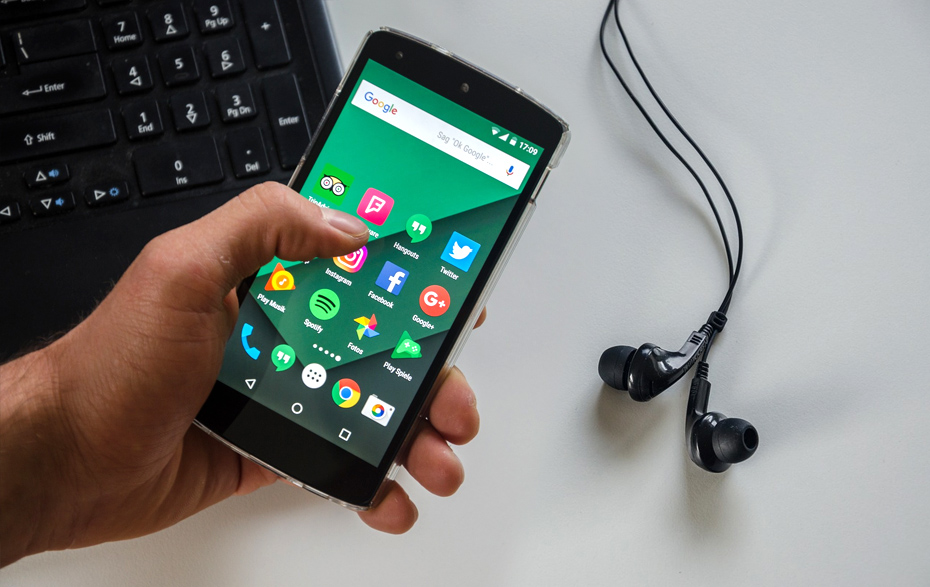 Foto: Hand mit Smartphone vor Laptop und Kopfhörern