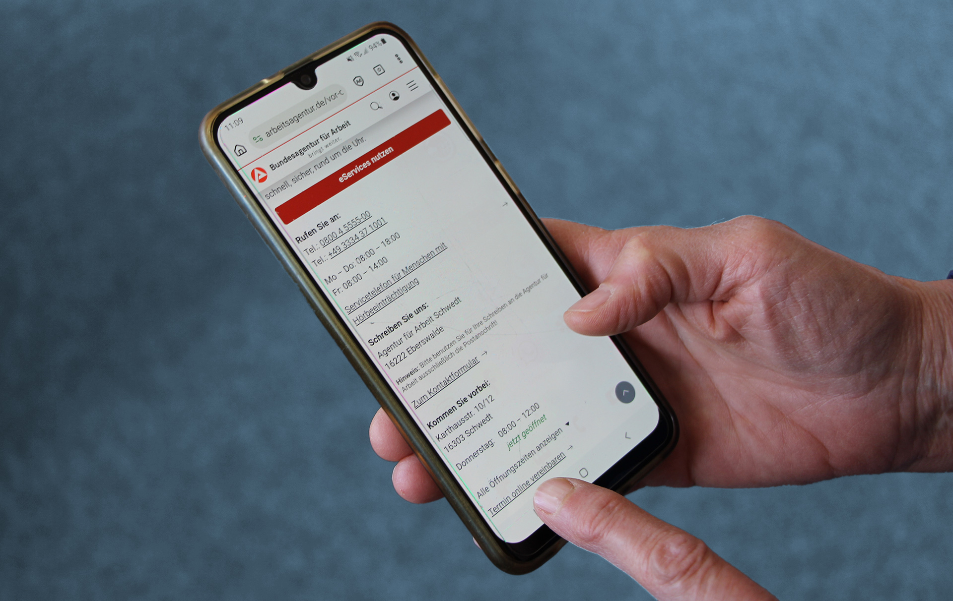 Foto: Hand mit Handy mit Fingerzeig auf den Link