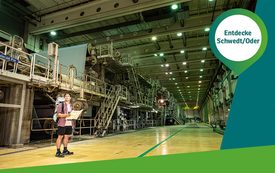 Foto: Wanderer vor der Papiermaschine und Pin „Entdecke Schwedt/Oder“