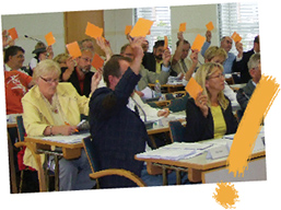 schräg gestelles Foto von einer Abstimmung in einer Stadtverordnetenversammlung mit gelbem Ausrufungszeichen schräg gestelles Foto von einer Abstimmung in einer Stadtverordnetenversammlung mit gelbem Ausrufungszeichen