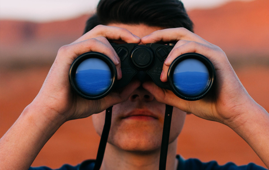 Foto: junger Mann schaut durch ein Fernglas