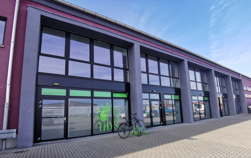 Foto: Haus mit Glasfassade und grünem Fahrradständer mit einem Fahrrad davor