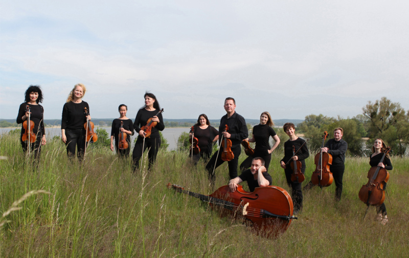 Foto: 11 Musiker und Musikerinnen mit ihren Streichinstrumenten in der Natur