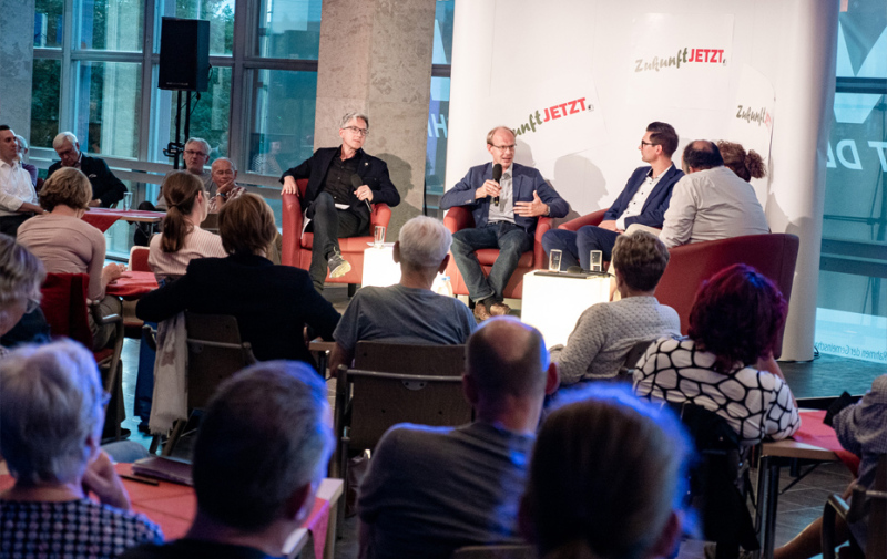 Foto: 5 Personen im Podium und Publikum drumherum